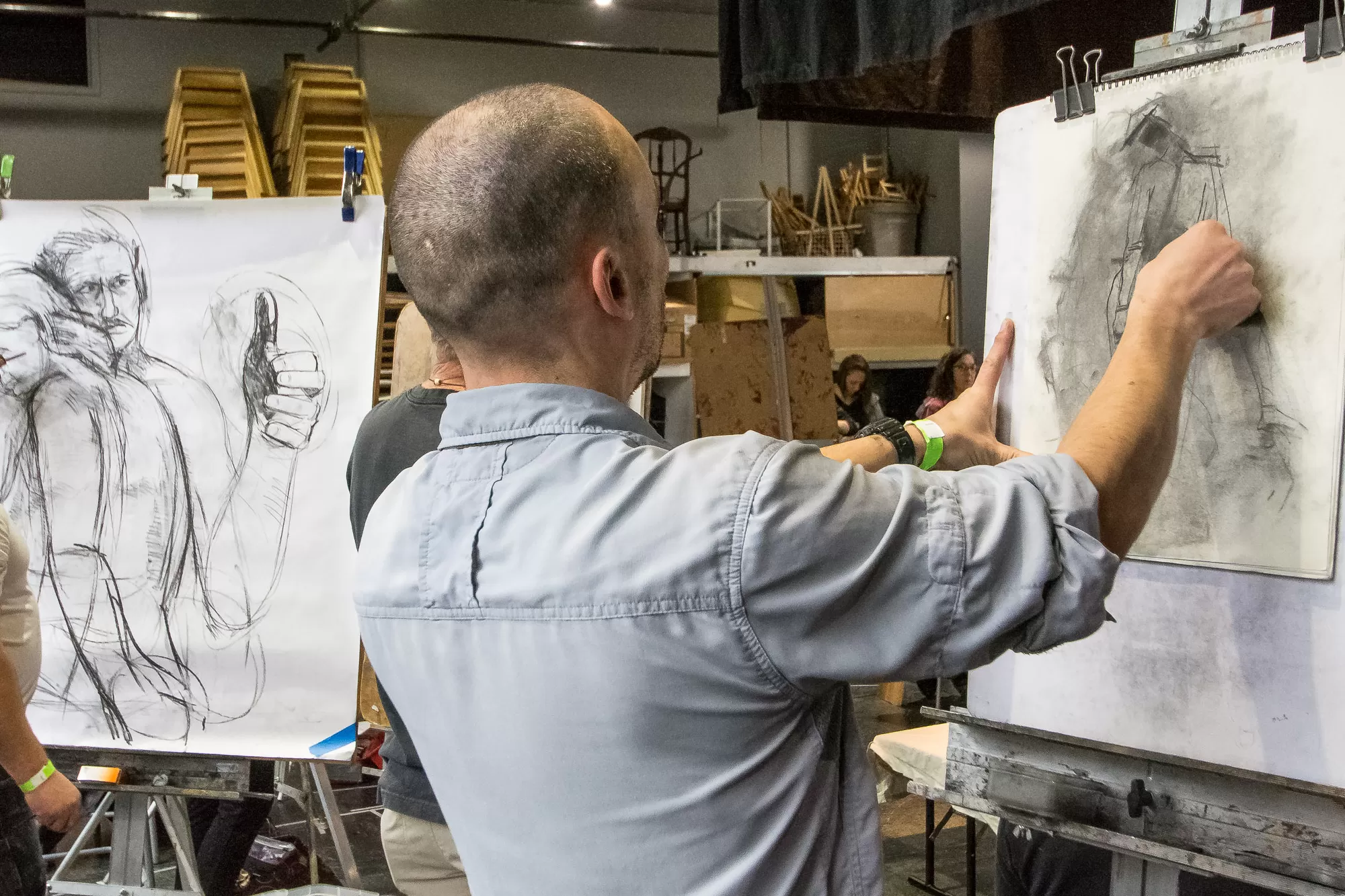 A man sketches on paper in cozy gage art studio, surrounded by colorful supplies and creative vibes.